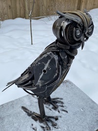 a metal owl sitting on a piece of snow
